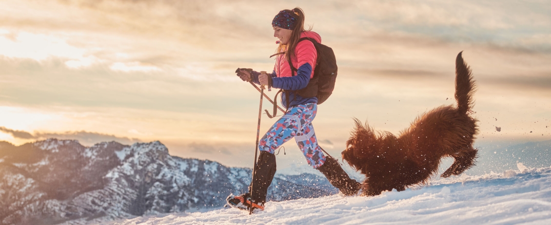 ragazza e il suo cane che corrono sulla neve in montagna in un trekking